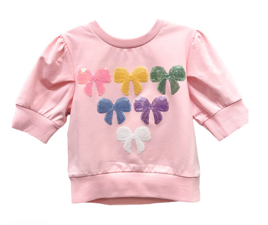 Pink Lulu Bebe girls’ blouse with puff sleeves and multicolored sequin bows, made from soft 95% cotton and 5% spandex fabric, displayed on a white background.