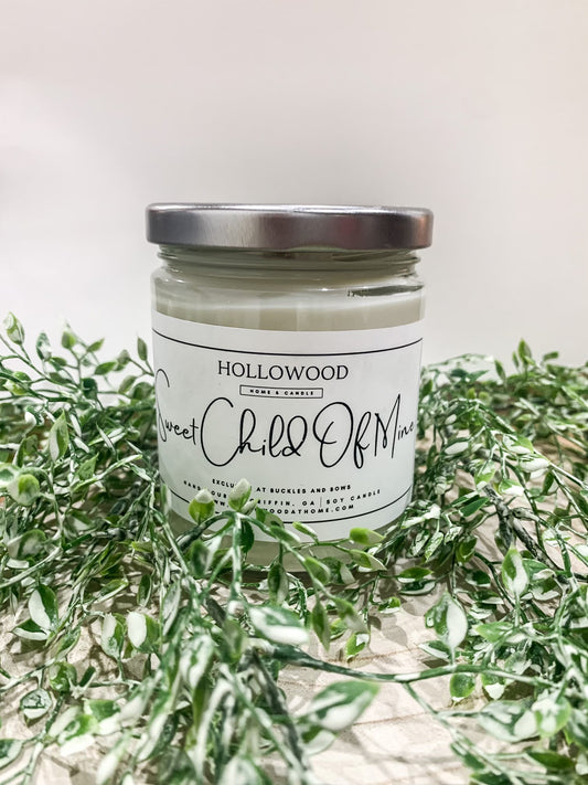 Exclusive Buckles & Bows candle in clear glass jar with black lid, available in mini, 8 oz, and 13 oz sizes, custom-made by Hollywood at Home.